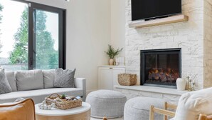 Una sala de estar moderna con chimenea, un sofá, otomanas y un televisor montado en la pared.