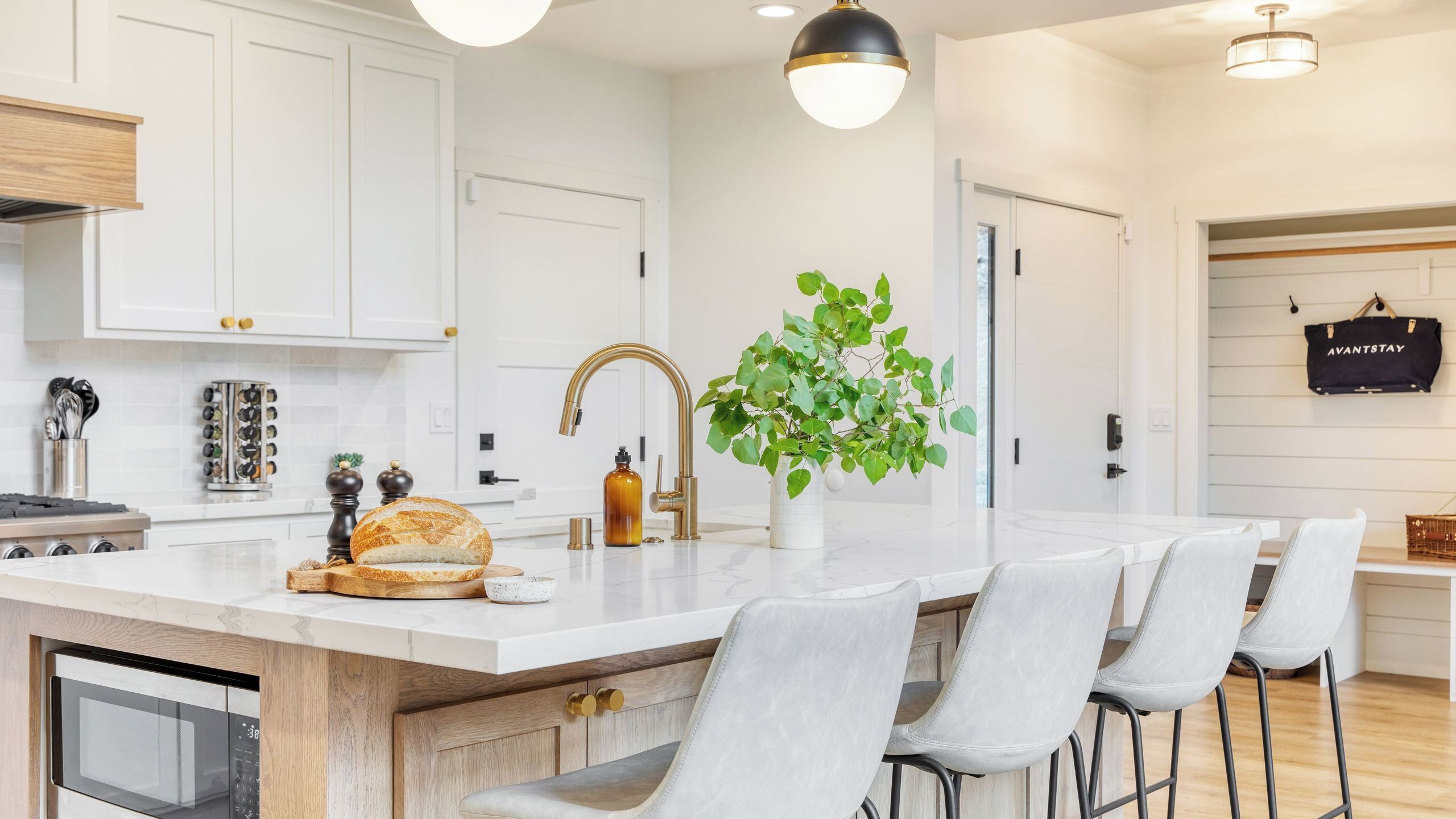 Une cuisine moderne avec des meubles blancs, un îlot central doté de tabourets de bar, une grande fenêtre et un sac suspendu portant l’inscription « AVANTSTAY ».