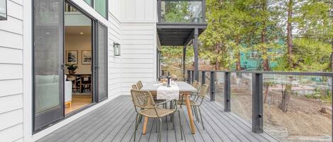 Terraza exterior con una mesa y sillas de comedor, una puerta de vidrio que da a una habitación y vistas de una zona boscosa.