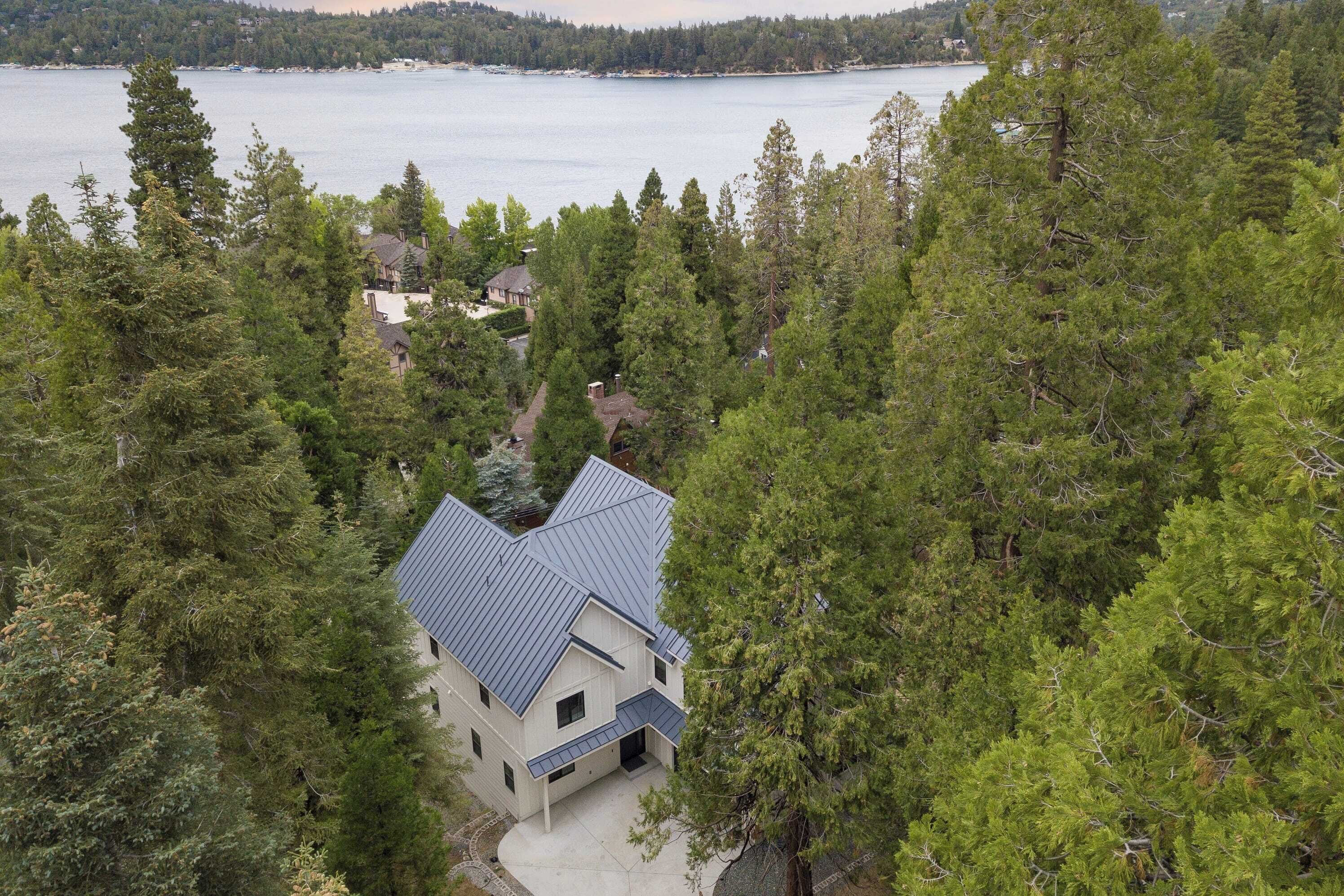 A house surrounded by dense forest with a view of a large body of water.