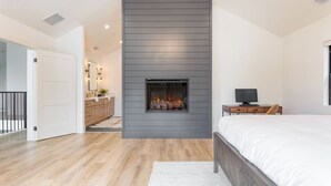 Un dormitorio con cama, televisión, chimenea y baño con lavamanos y espejo.