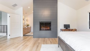 A bedroom with a bed, a TV, a fireplace, and a bathroom with a sink and mirror. - Luxury Retreat, 5mins to the Lake Game Room + Fire Pit Howlite by Avantstay (Lake Arrowhead)