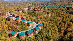 Un albergue con varias construcciones, un camino sinuoso y un paisaje montañoso cubierto de bosque.