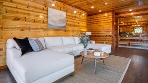 Interior moderno de una cabaña de troncos con un sofá modular, una mesa de centro redonda y un ventilador de techo.