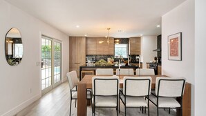 A modern kitchen with a central island, dining table with chairs, and a large window. - Yellowjacket by Avantstay Entertainers Yard 10min to Downtown (Palm Springs)