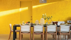A dining table set with chairs, a pitcher, a bowl of fruit, and decorative items against a yellow wall.