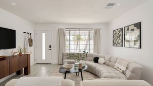 A living room with a sectional sofa, a coffee table, a TV, and a large window with curtains. - Yellowjacket by Avantstay Entertainers Yard 10min to Downtown (Palm Springs)