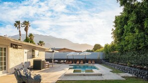 Ein Poolbereich mit Liegestühlen, einer Steinmauer und einem Berg im Hintergrund.