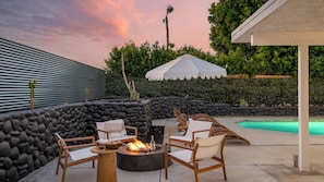 Une terrasse extérieure avec un foyer, des chaises longues et une piscine.