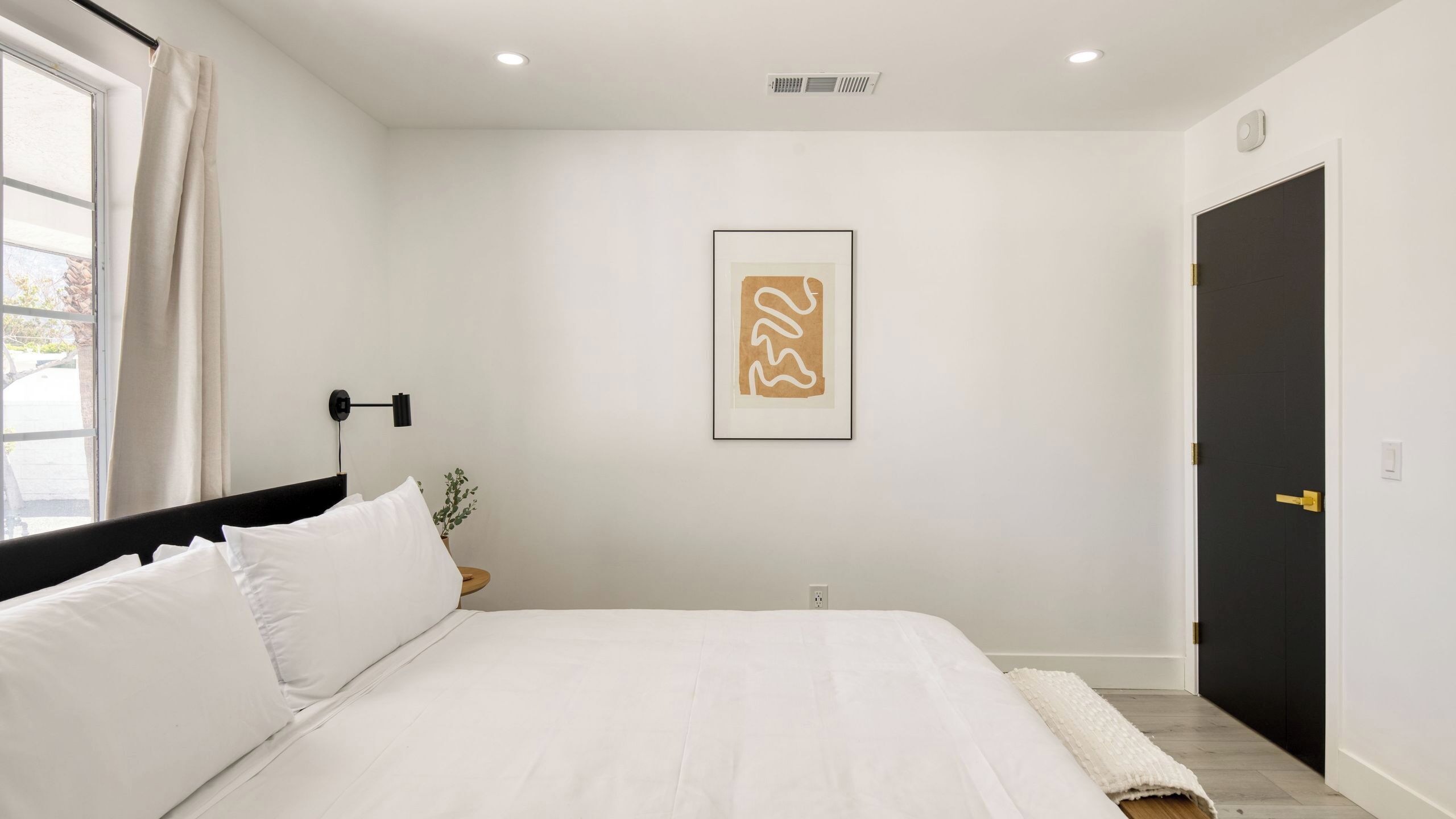 Un dormitorio con cama, una lámpara de pared, una puerta y una obra de arte enmarcada.