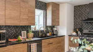 Eine moderne Küche mit Holzausstattung, schwarzem Fliesenrückwand, Spülbecken aus Edelstahl und einem Herd.