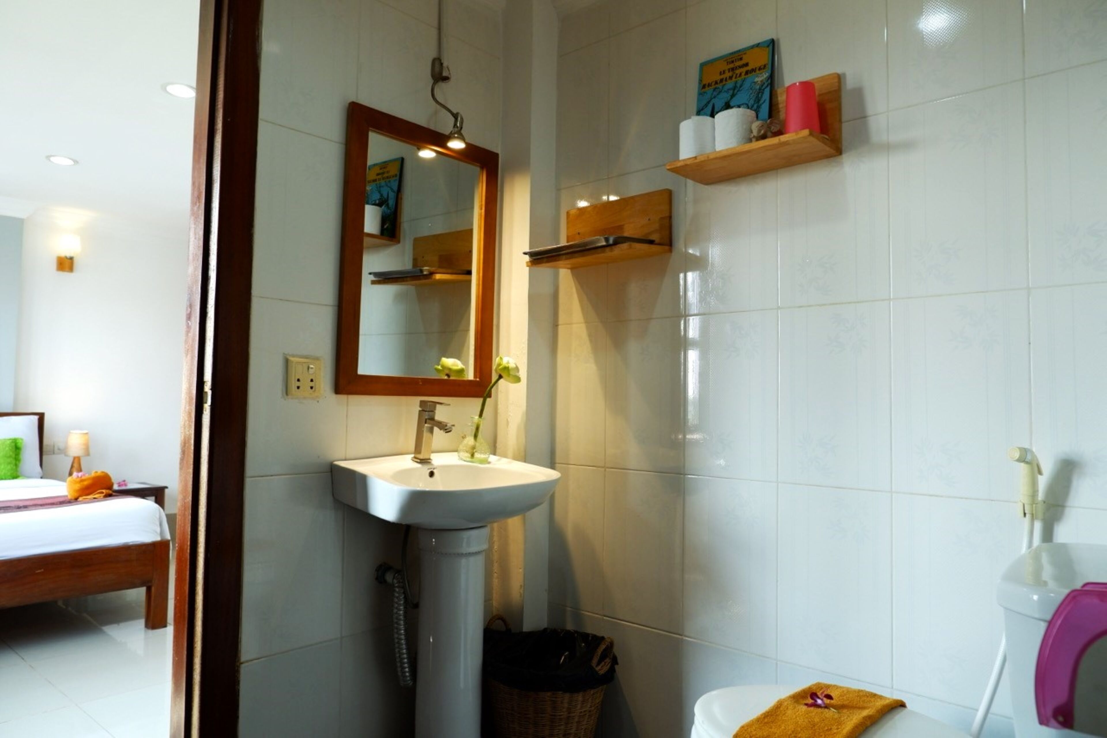 A bathroom with a sink, mirror, and toilet. There is a shelf with toiletries and a basket.