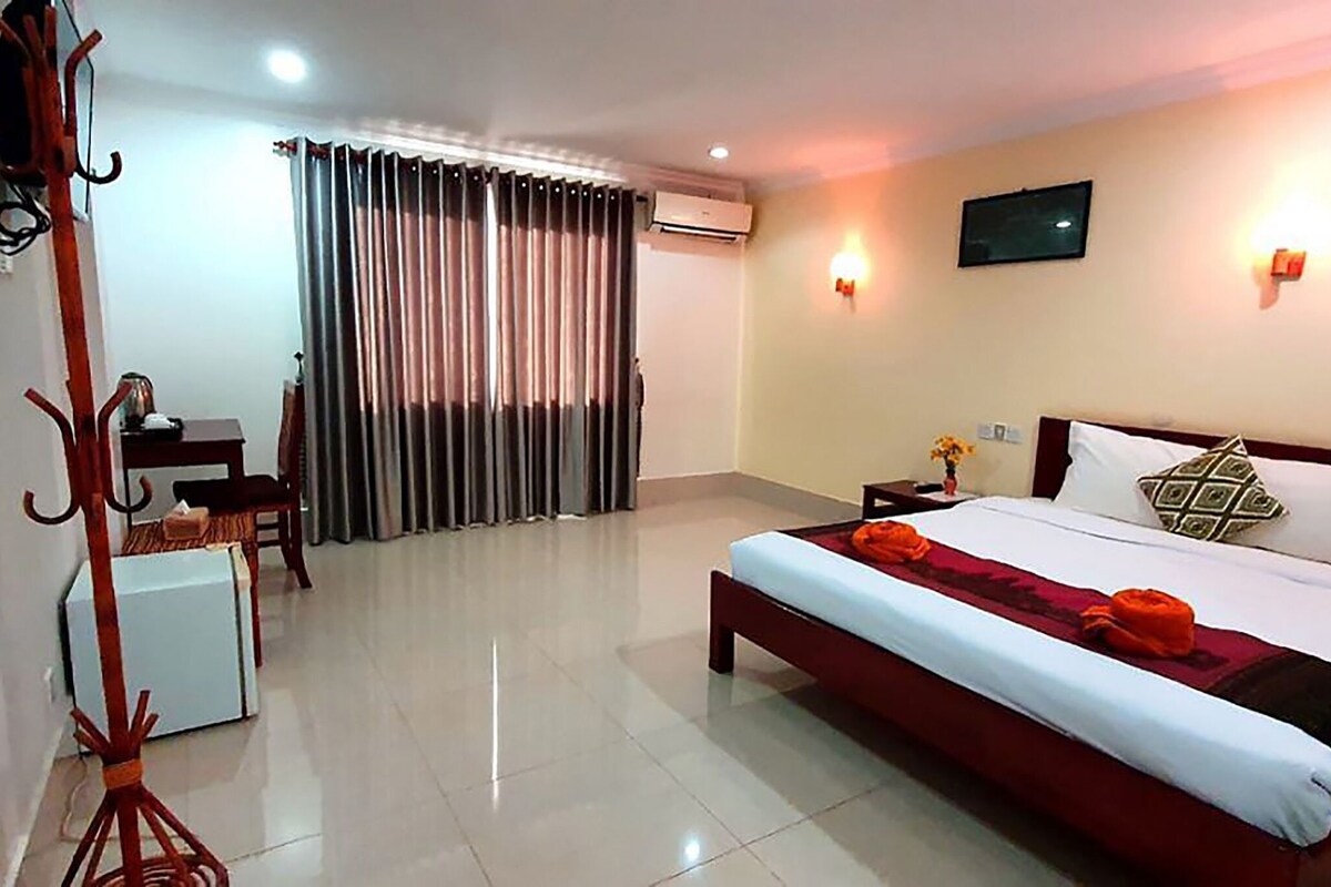 A hotel room with a bed, a desk, a chair, a coat rack, and a television.