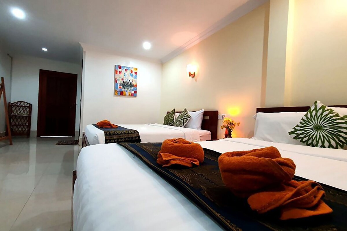 A hotel room with two beds, a wooden chair, a painting on the wall, and a nightstand with a lamp.