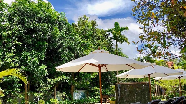 A pool area with lounge chairs and umbrellas, surrounded by lush greenery. - Nary Villa (Siem Reap)