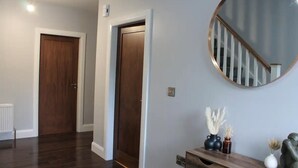 A hallway with wooden doors, a round mirror, and a console table with decorative items. - Forest View House - Private Hot Tub (Coleraine)