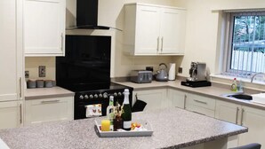 A modern kitchen with white cabinets, a black stove, and a granite countertop. - Forest View House - Private Hot Tub (Coleraine)