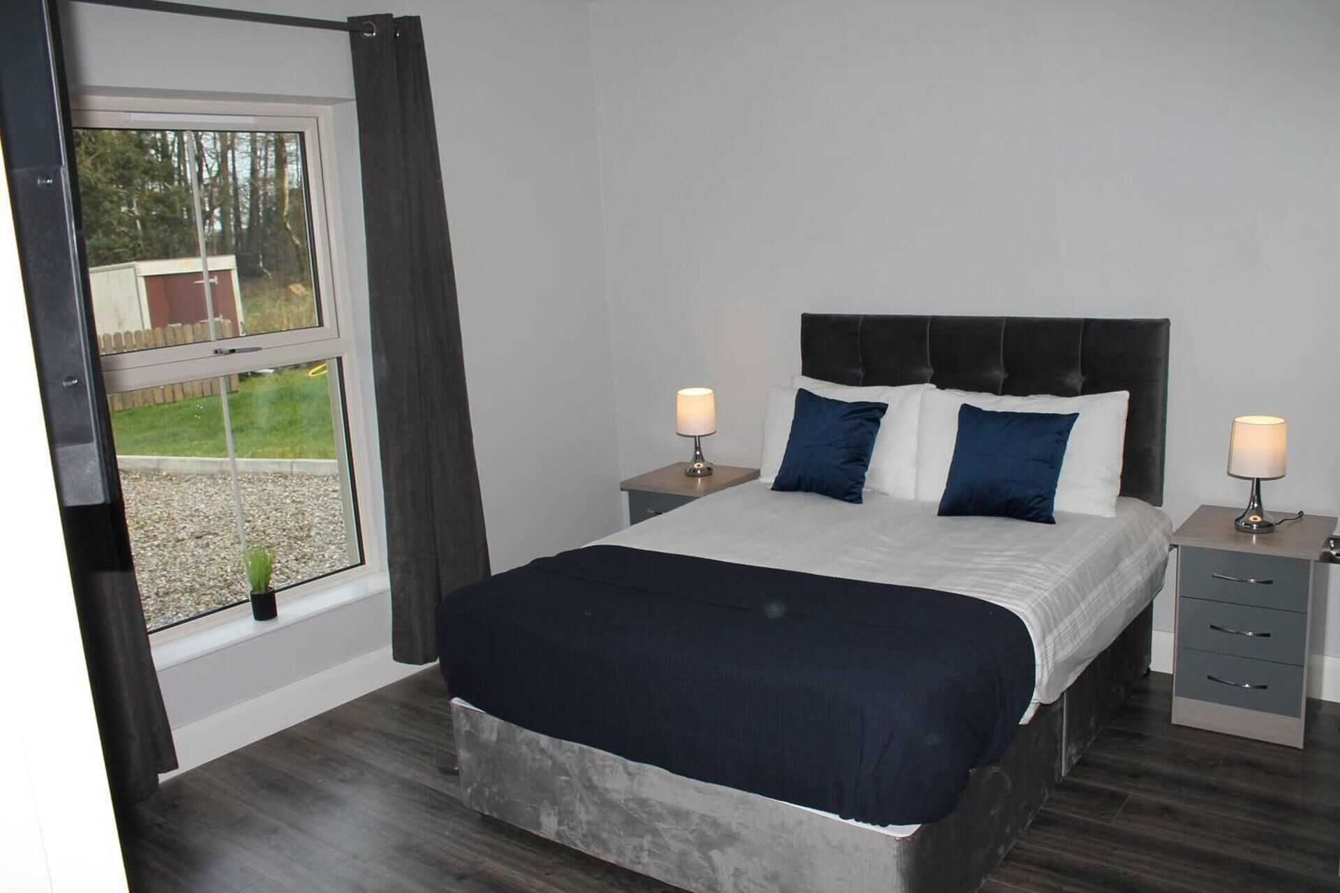 Een slaapkamer met een bed, twee nachtkastjes met lampen, een raam met gordijnen en uitzicht op de omgeving.