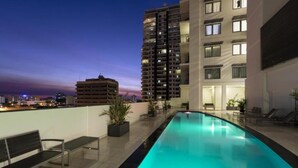 Une piscine située sur le toit, offrant une vue sur les toits de la ville au crépuscule.