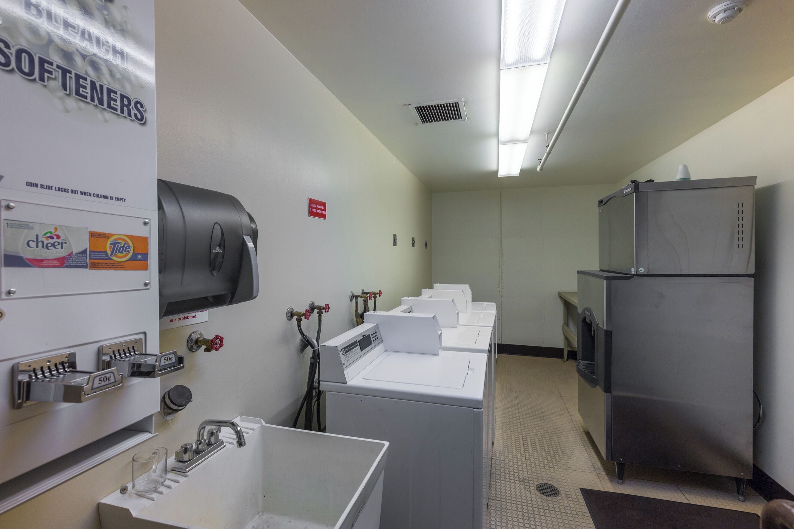 A laundry facility with multiple washing machines, a coin-operated dryer, and a sink with hand soap dispensers.