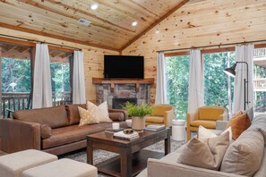 A cozy cabin interior with a stone fireplace, leather sofas, and a flat-screen TV.