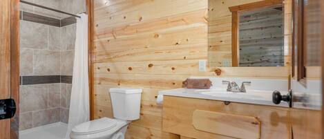 A wooden cabin bathroom with a shower, toilet, and sink.
