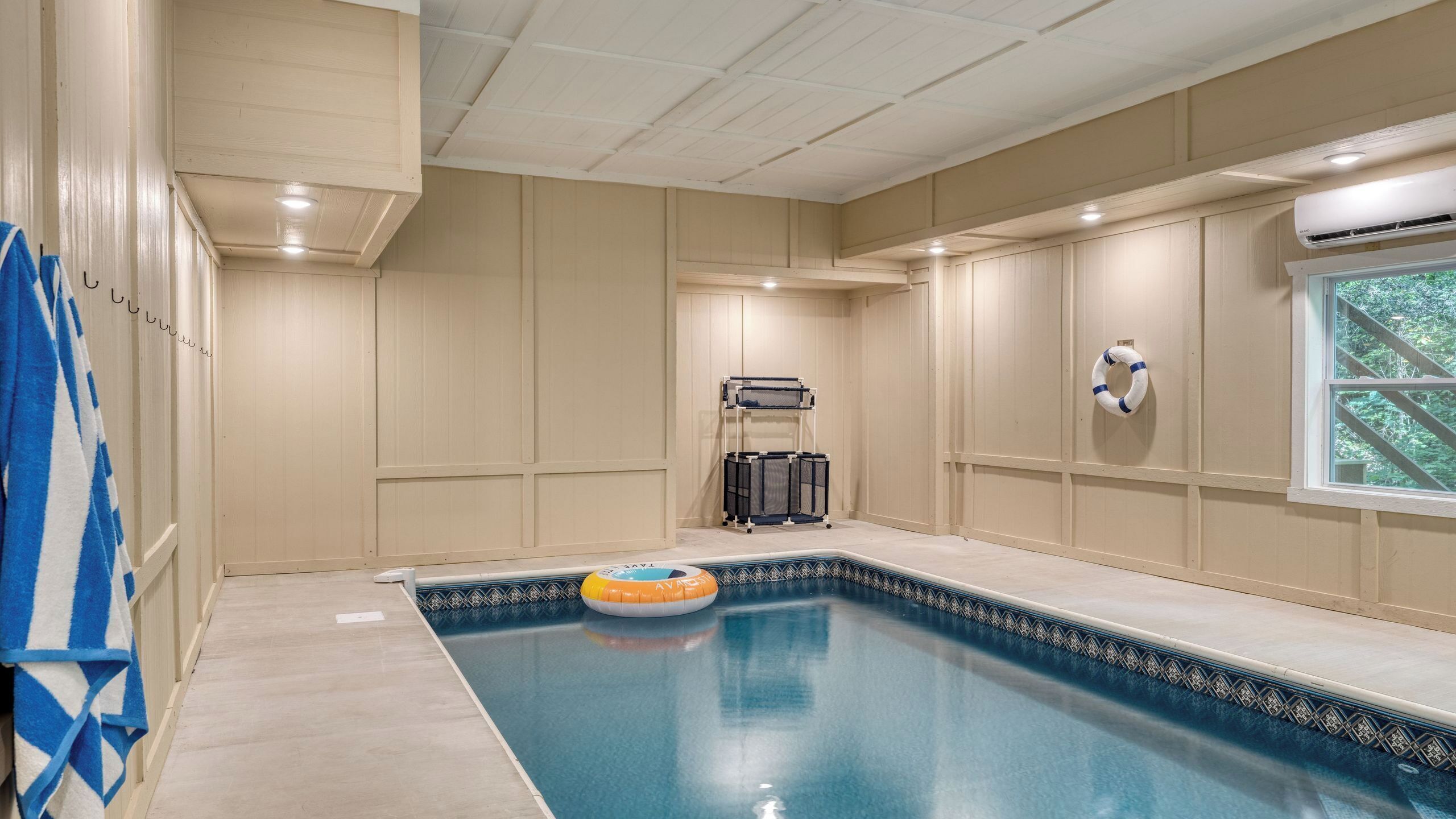 A swimming pool with a lifebuoy, a window with a view, and a ceiling fan.