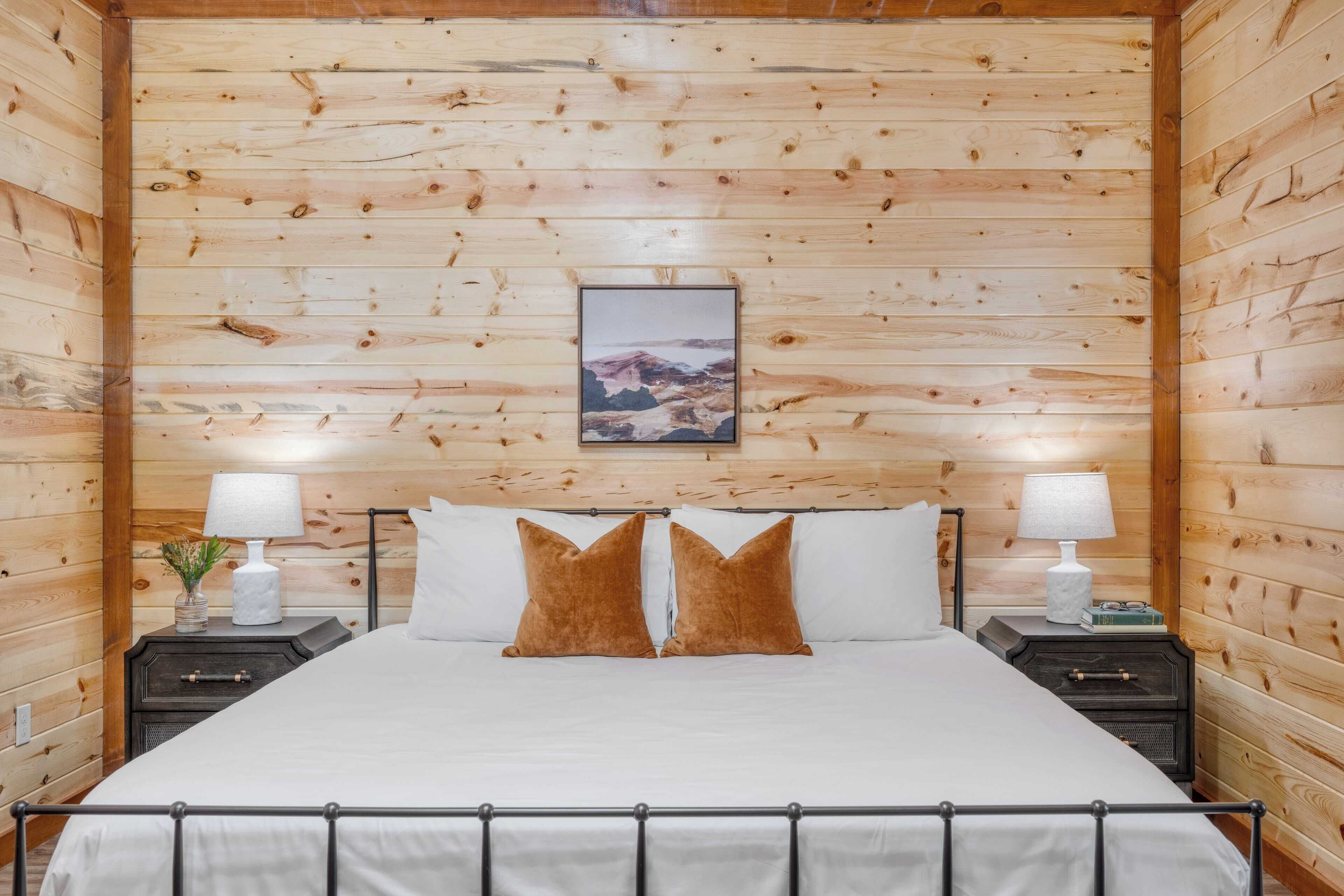 A wooden-paneled room with a bed, two bedside tables, and a framed picture on the wall.