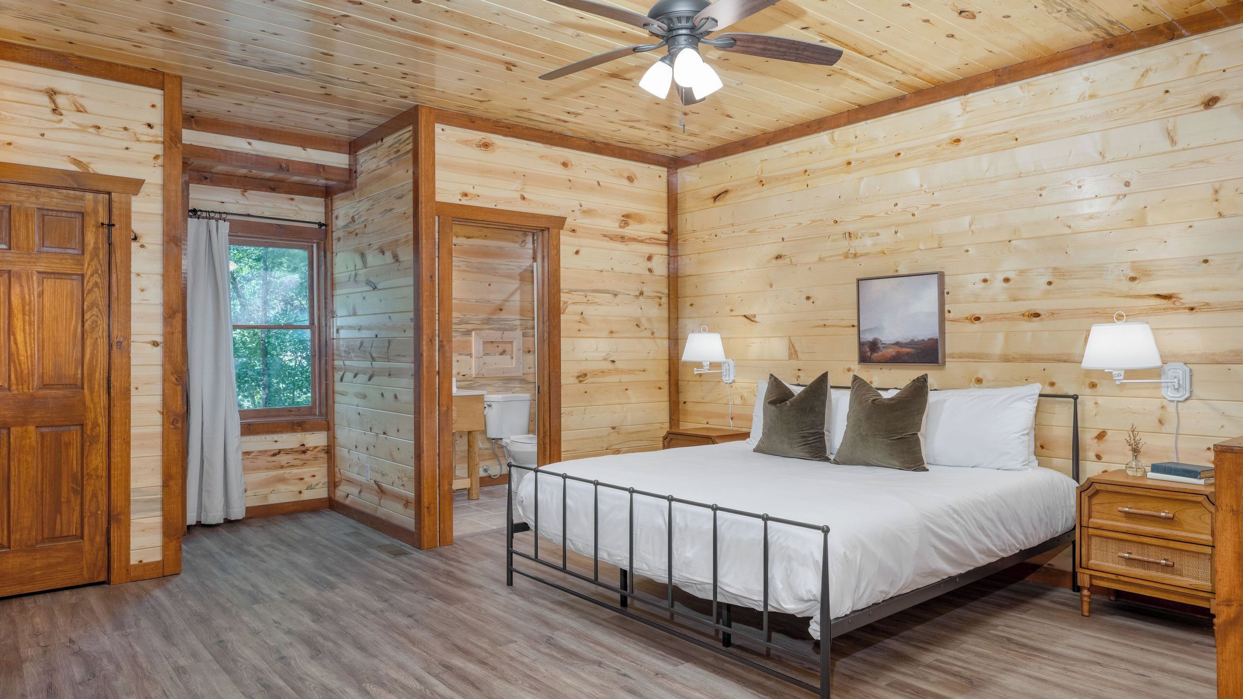 Quarto de cabana de madeira com cama, mesas de cabeceira, ventilador de teto e janela.
