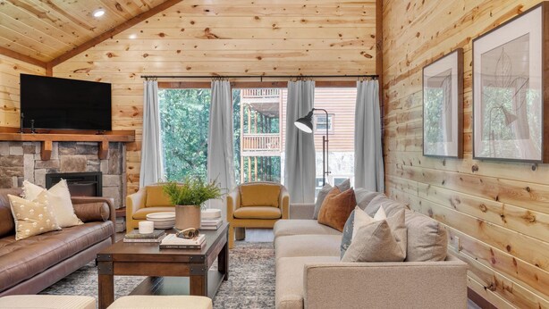 A cozy cabin interior with a stone fireplace, leather sofas, a coffee table, and framed artwork on the walls.