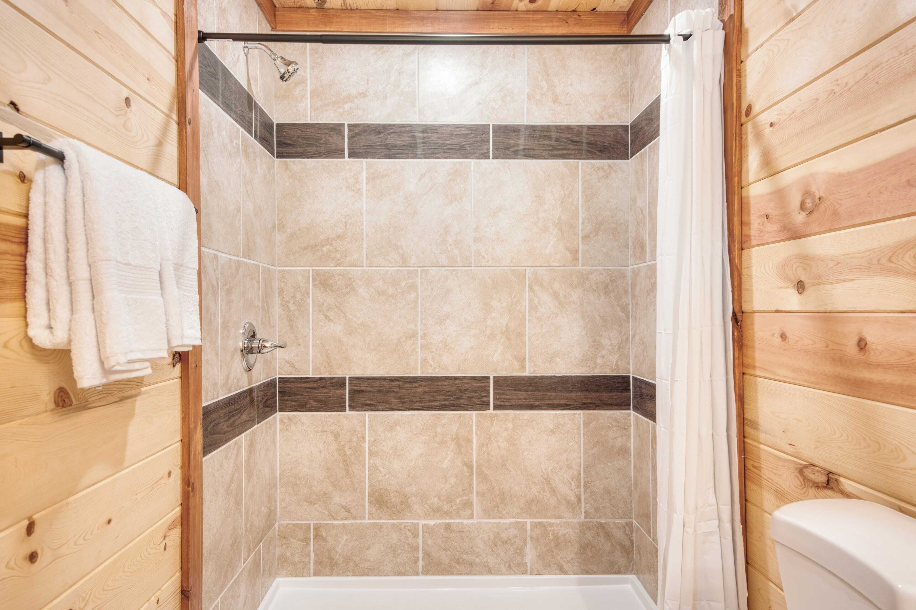 A shower with wooden panel walls, a white bathtub, and a towel rack.