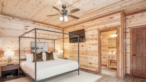 Un lit à baldaquin avec un téléviseur fixé au mur, un plancher en bois et un ventilateur de plafond.