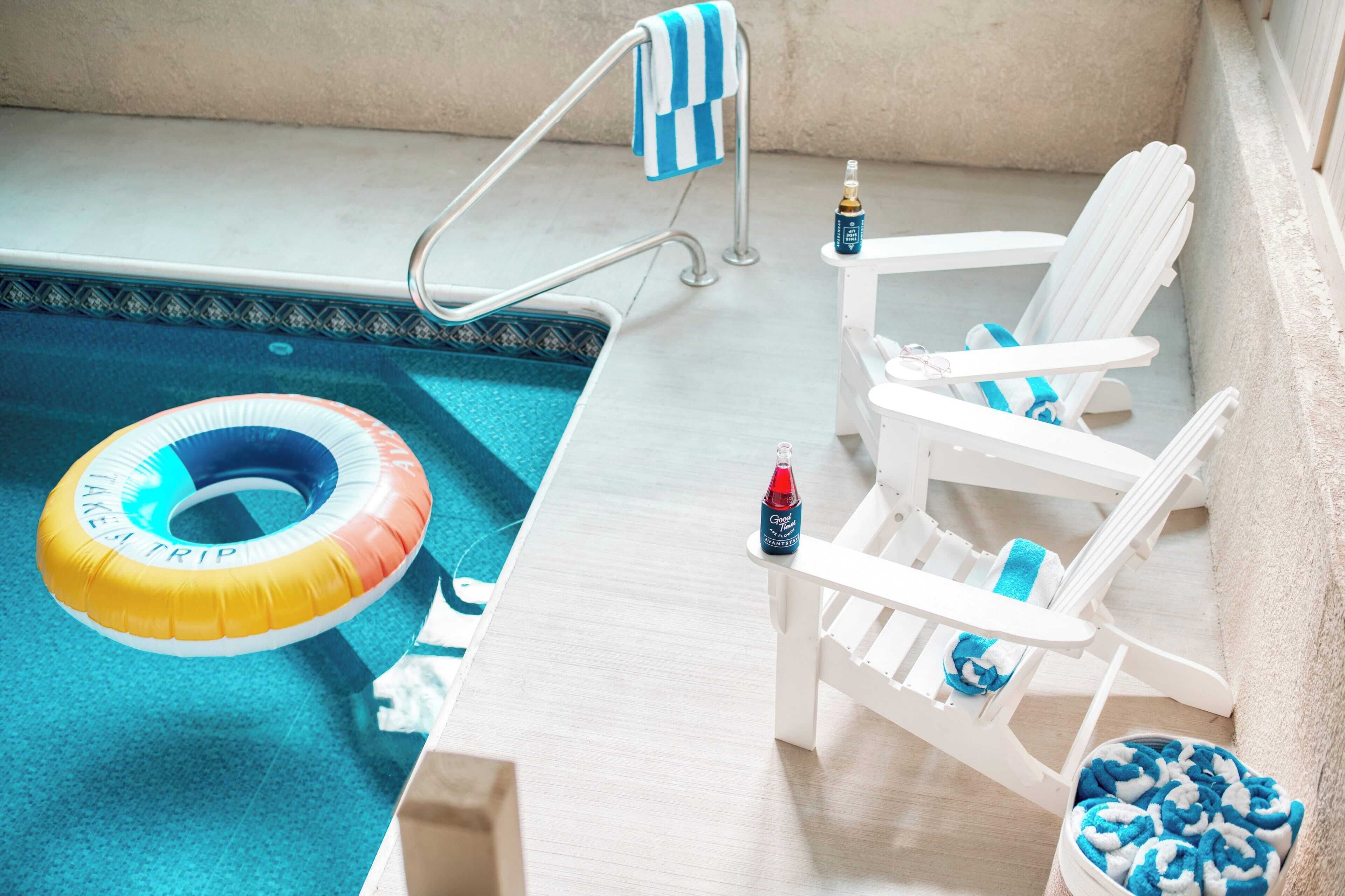 A pool area with a floating ring, a bottle, and a chair with a towel.