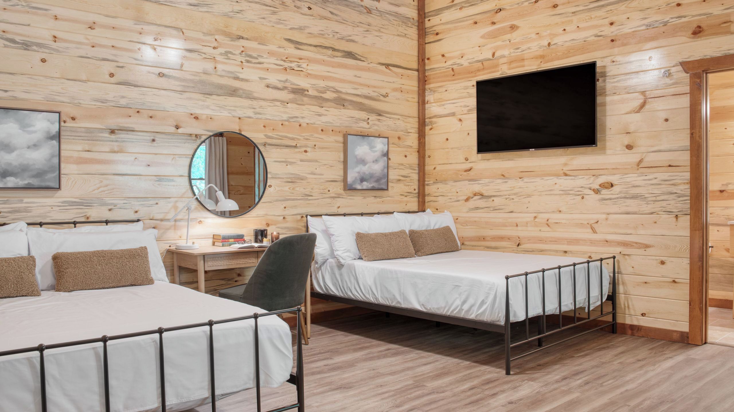 Una habitación tipo cabaña con dos camas, un escritorio, una silla, un espejo y un televisor.
