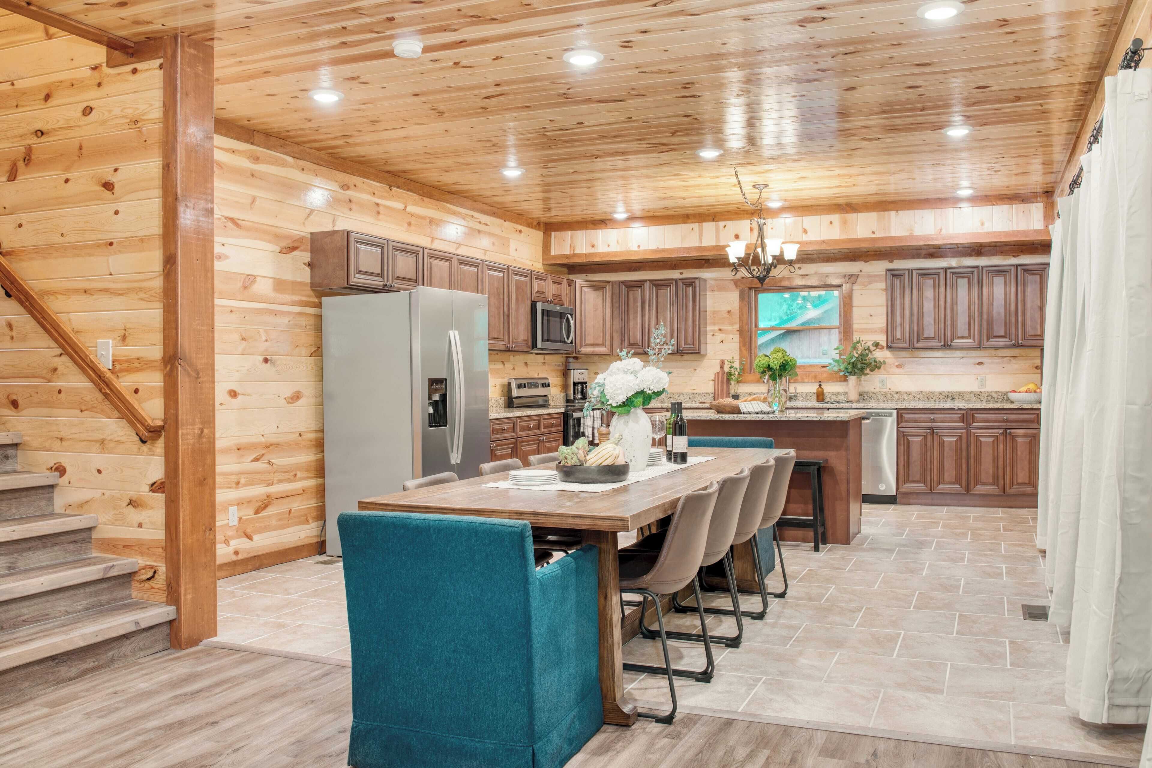 A modern kitchen with wooden walls, a central island, and a dining area with teal chairs.