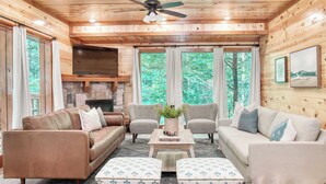 L’intérieur d’un chalet accueillant, avec un plafond en bois, une cheminée, un canapé, deux fauteuils et une table basse.