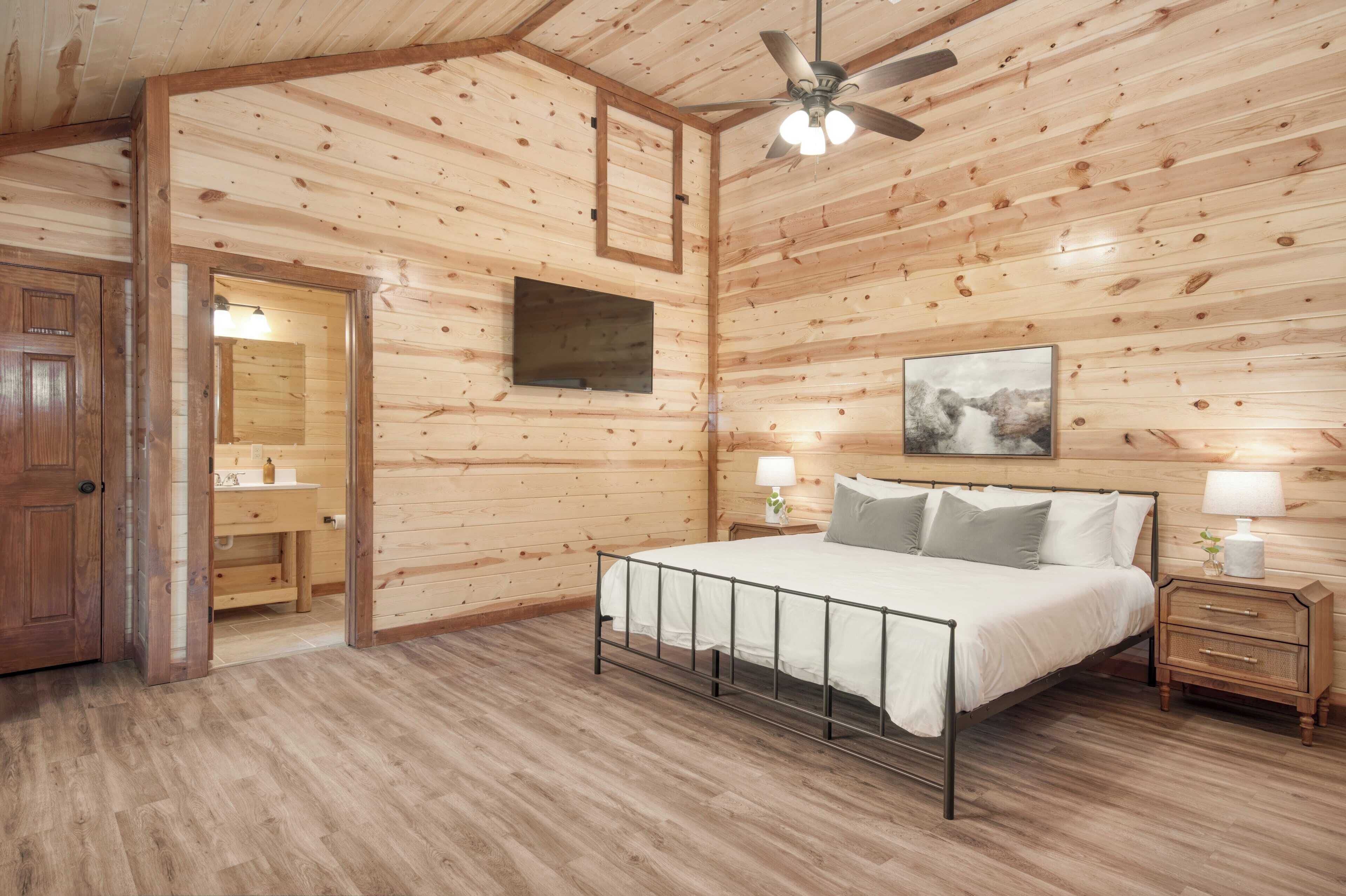 A bedroom with a wooden ceiling, a bed with white bedding, a nightstand with a lamp, and a mounted TV.