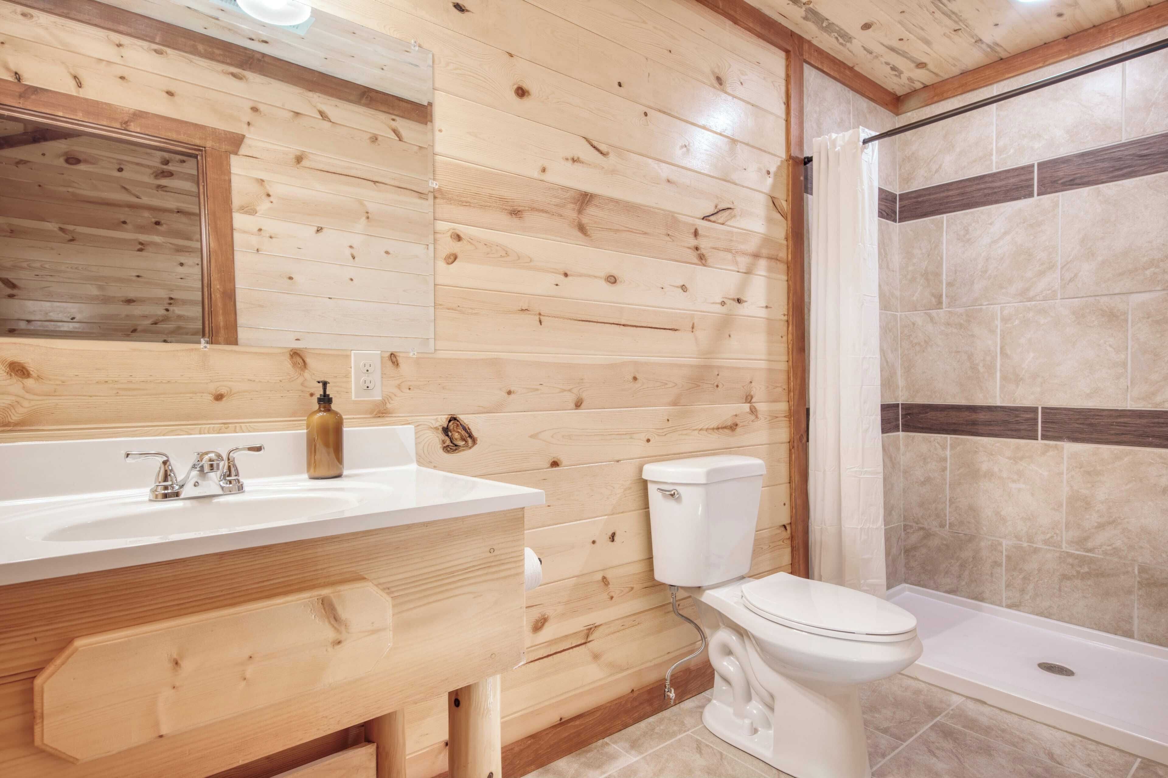 A wooden-paneled bathroom with a white sink, a toilet, and a shower area.