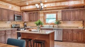 A kitchen with wooden cabinetry, a central island, a microwave, a dishwasher, and a chandelier.
