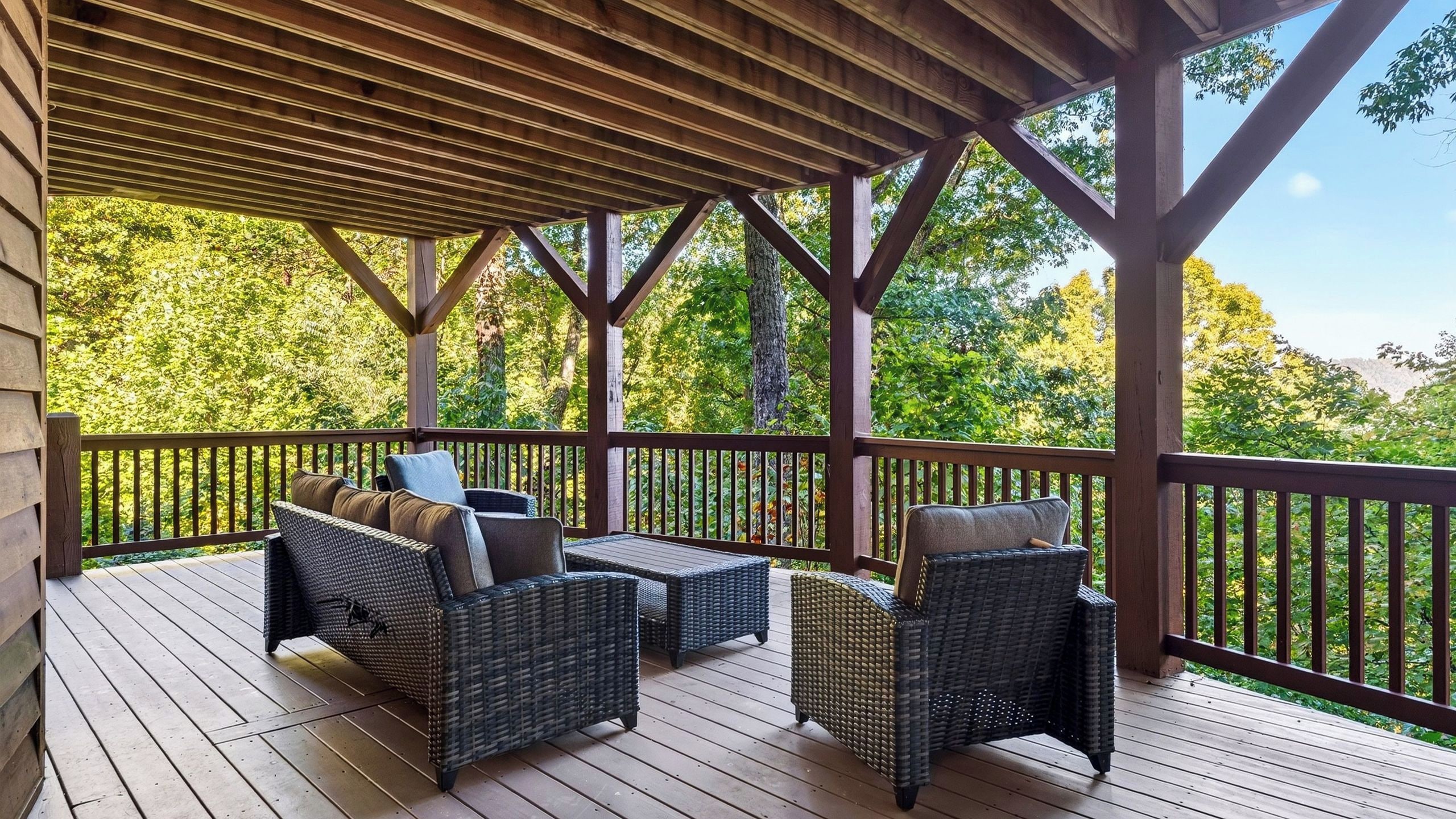 Une terrasse extérieure couverte, aménagée avec des meubles en osier et dotée d’une rambarde.