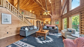 A log cabin interior with a staircase, two sofas, a coffee table, and a view of the outdoors.