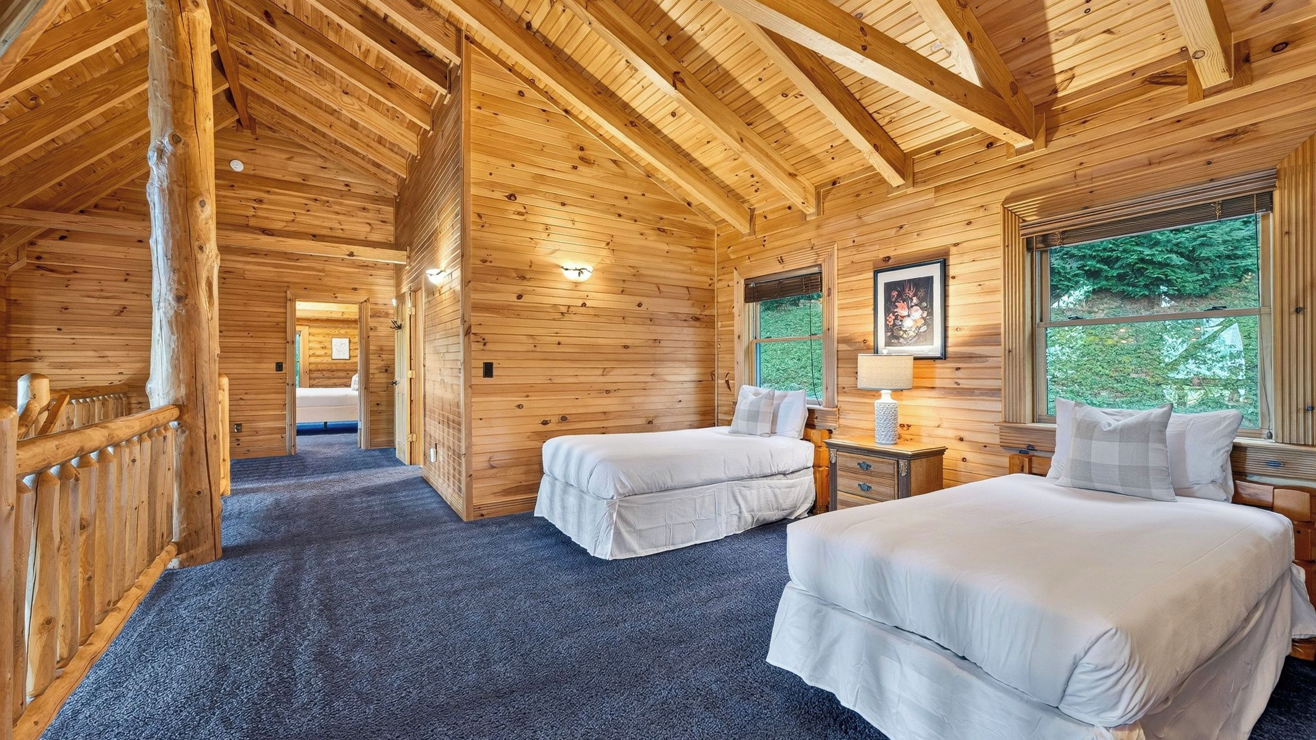 A wooden cabin with two beds, a small table, and a window with a view of greenery.