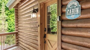 A wooden cabin with a door, a welcome sign, and a mailbox.