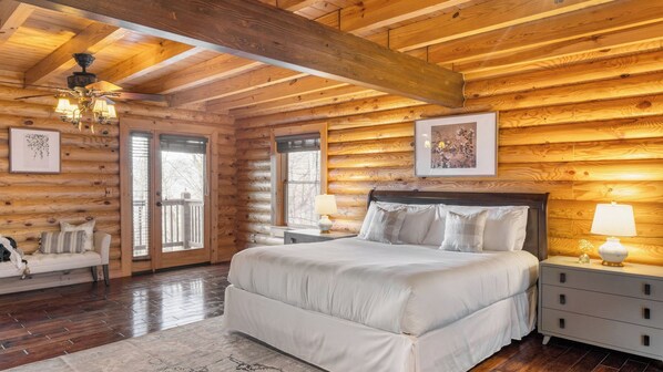 Un dormitorio tipo cabaña de madera con una cama grande, techo de madera y vistas por la puerta.