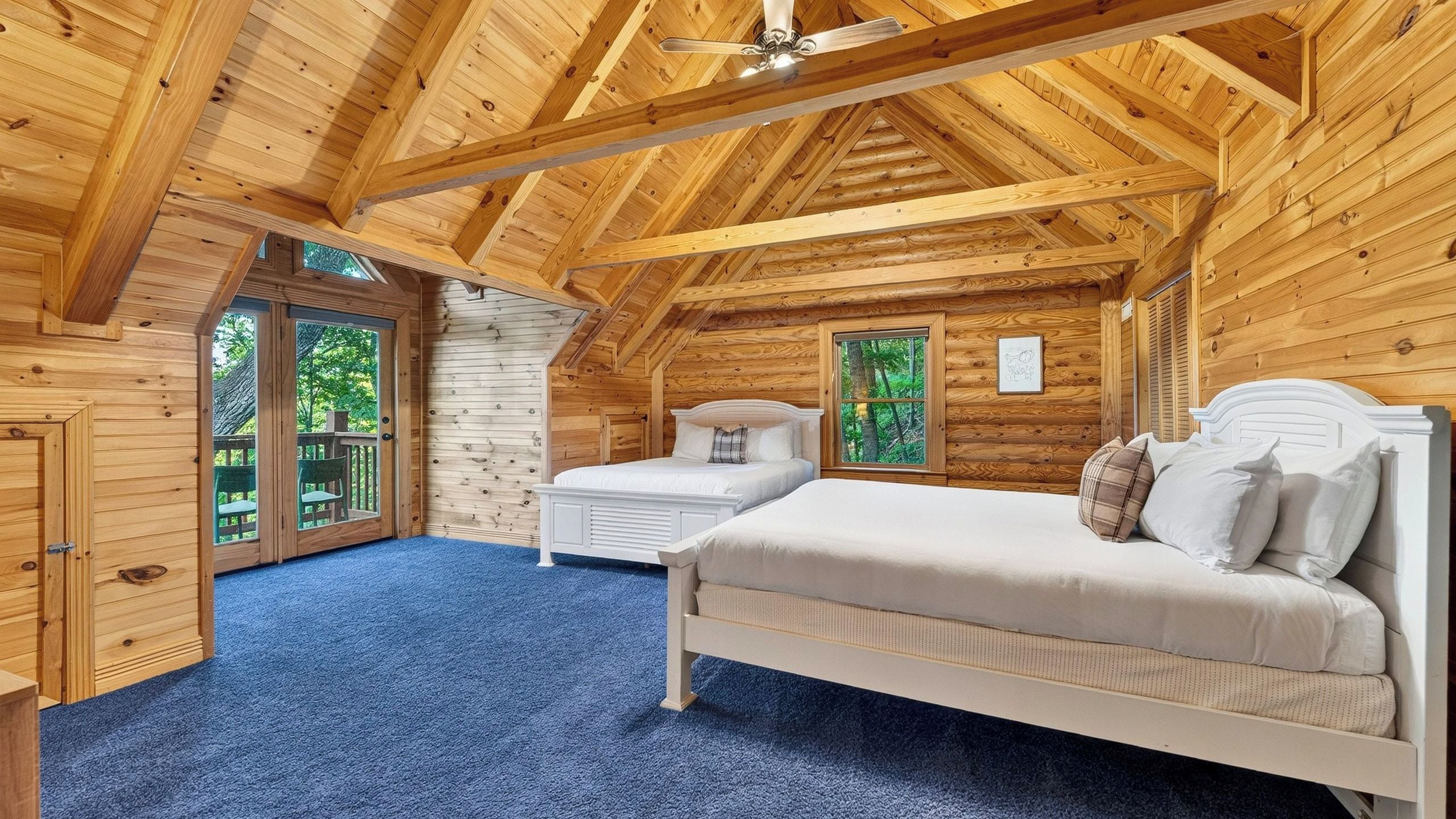 Un dormitorio de cabaña de madera con cama, mesita de noche y ventana con vista a árboles.