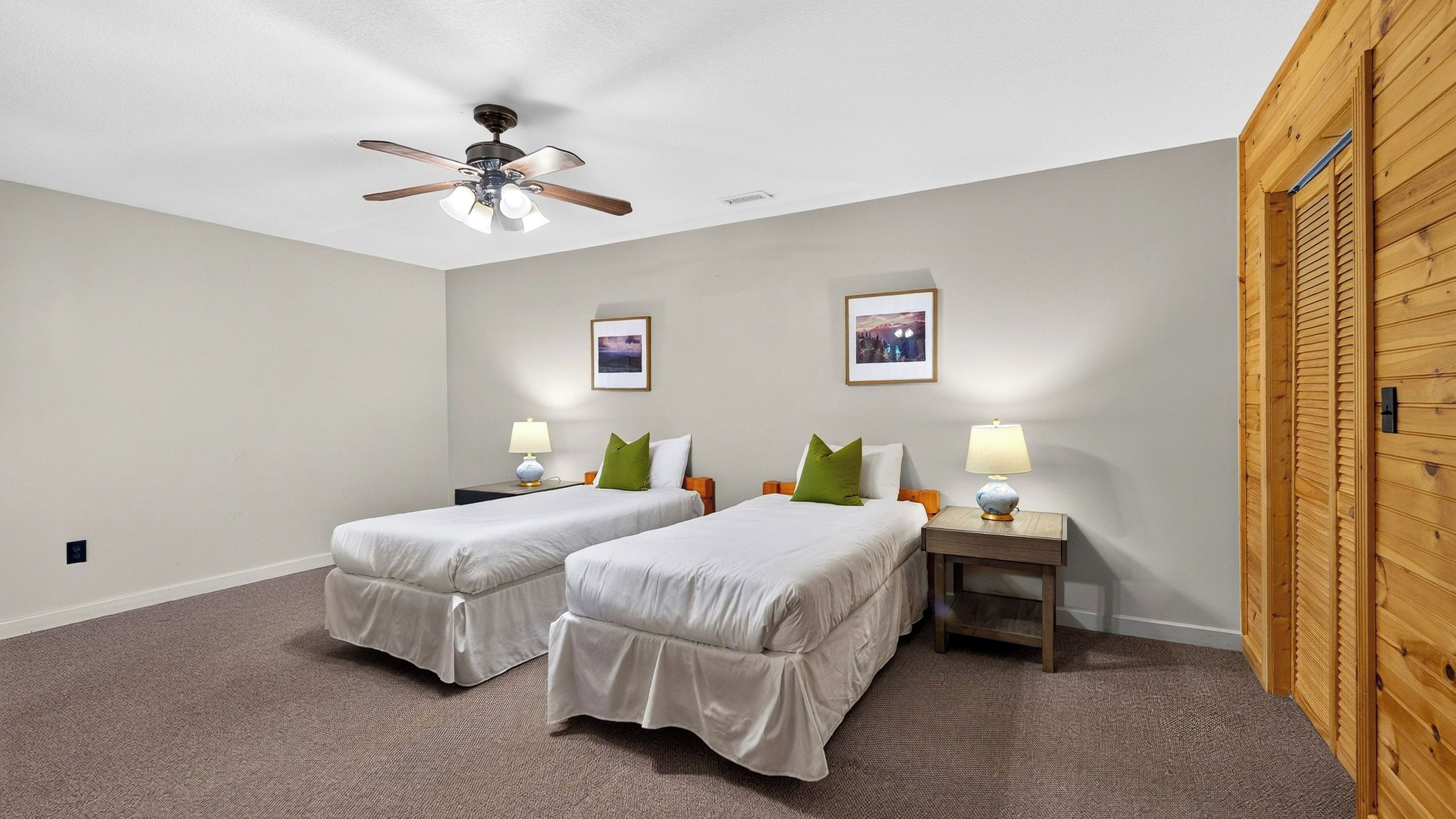 Una habitación con dos camas individuales, un ventilador de techo, dos mesitas de noche con lámparas y dos cuadros en la pared.