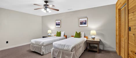 Una habitación con dos camas individuales, un ventilador de techo, dos mesitas de noche con lámparas y dos cuadros en la pared.