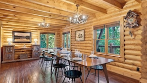 A log cabin interior with a dining area, wooden walls, and large windows. - Leyland by Avantstay Cabin Mansion w/ Views (Asheville)