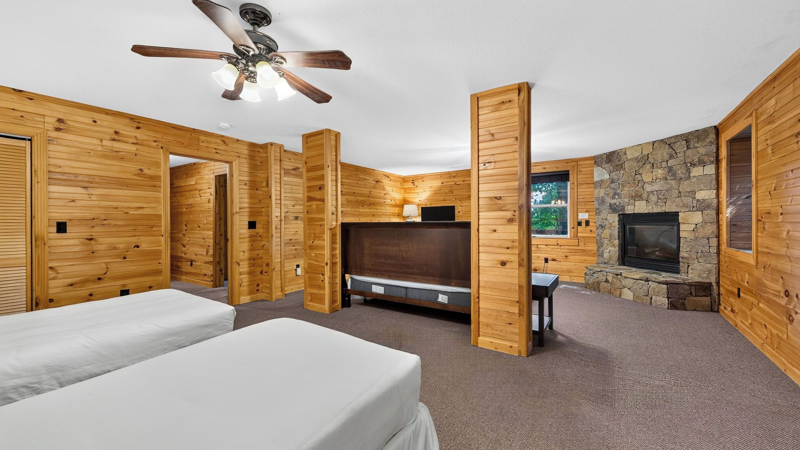 A room with wooden walls, a ceiling fan, a fireplace, and a bed.