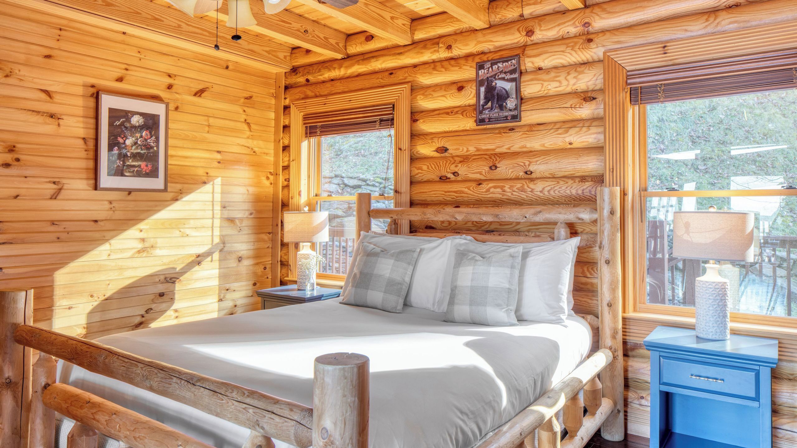 A wooden cabin bedroom with a bed, a nightstand, a lamp, and a framed picture on the wall.